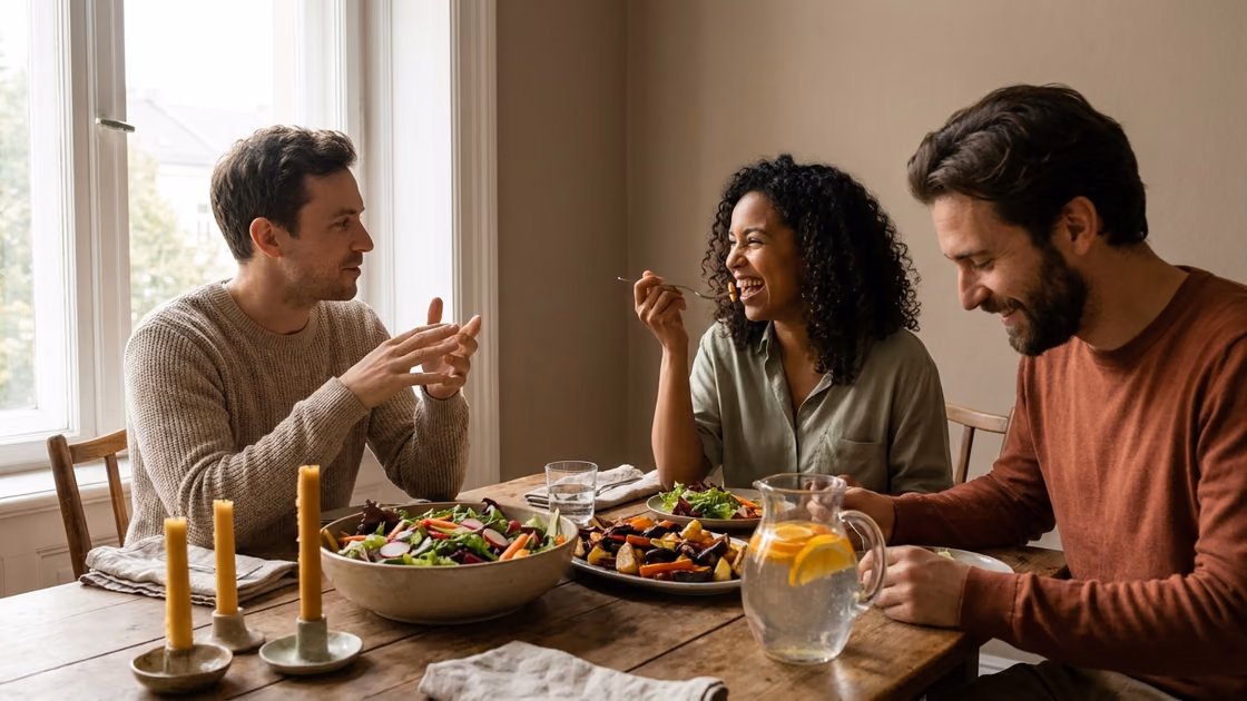 Three friends sharing a colorful healthy dinner around a wooden table, laughing in warm evening light